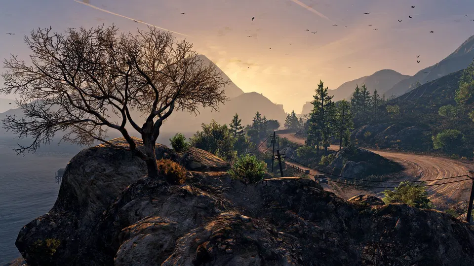 GTA 5: Osamělý strom na skalnatém útesu, vedle klikatá cesta a západ slunce nad horami.