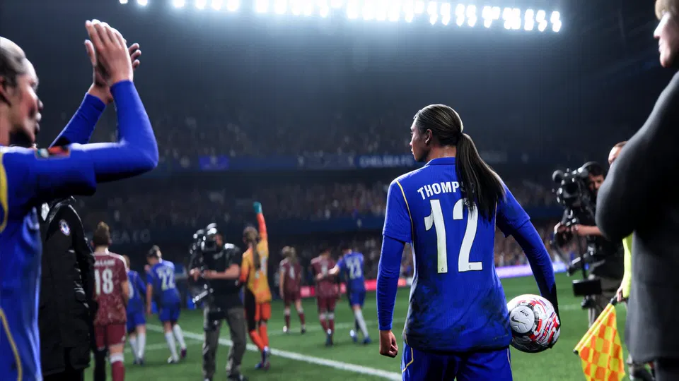 EA Sports FC 27: hráčka v modrém dresu s číslem 12 a jménem THOMP jde na hřiště s míčem pod paží.