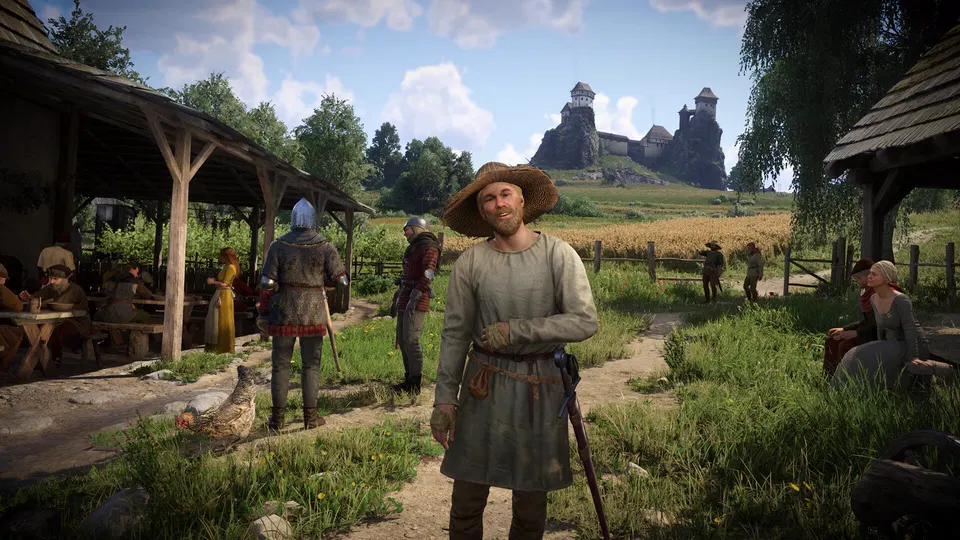Kingdom Come: Deliverance II: muž v klobouku stojí na vesnické cestě, v pozadí hrad a lidé u stánků.