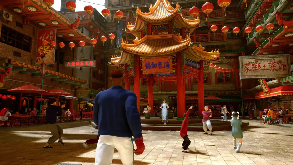 Street Fighter 6: čínské náměstí s červenou pagodou, lampiony a postavou v modré bundě zezadu