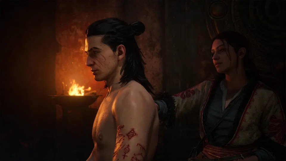 The Blood of Dawnwalker: svalnatý muž s tetováním a rudými znaky sedí u ohně, vedle něj žena v kimonu